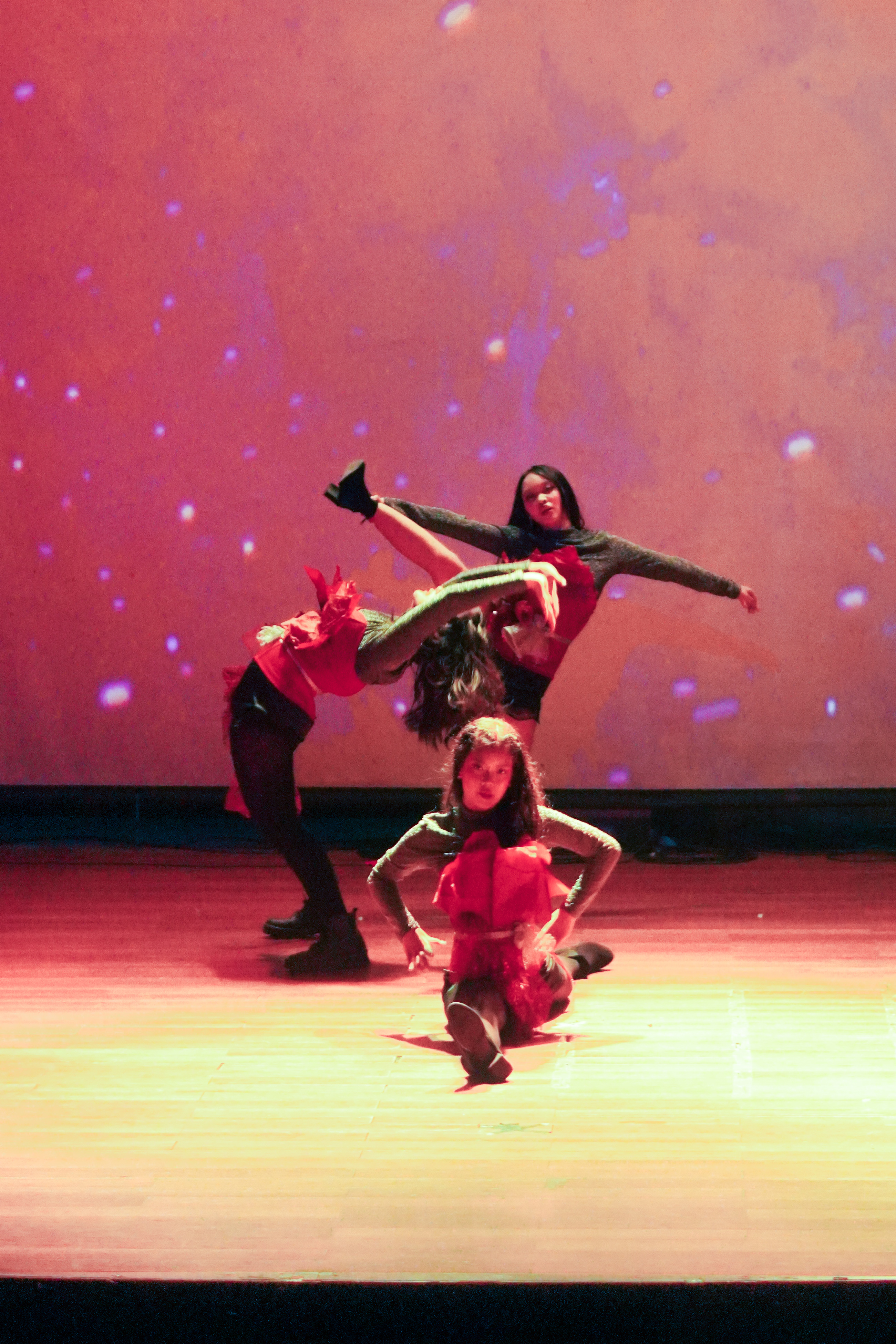 Dancers in a dynamic formation under deep red stage lighting with a starry projection backdrop at Jalantari 4.0