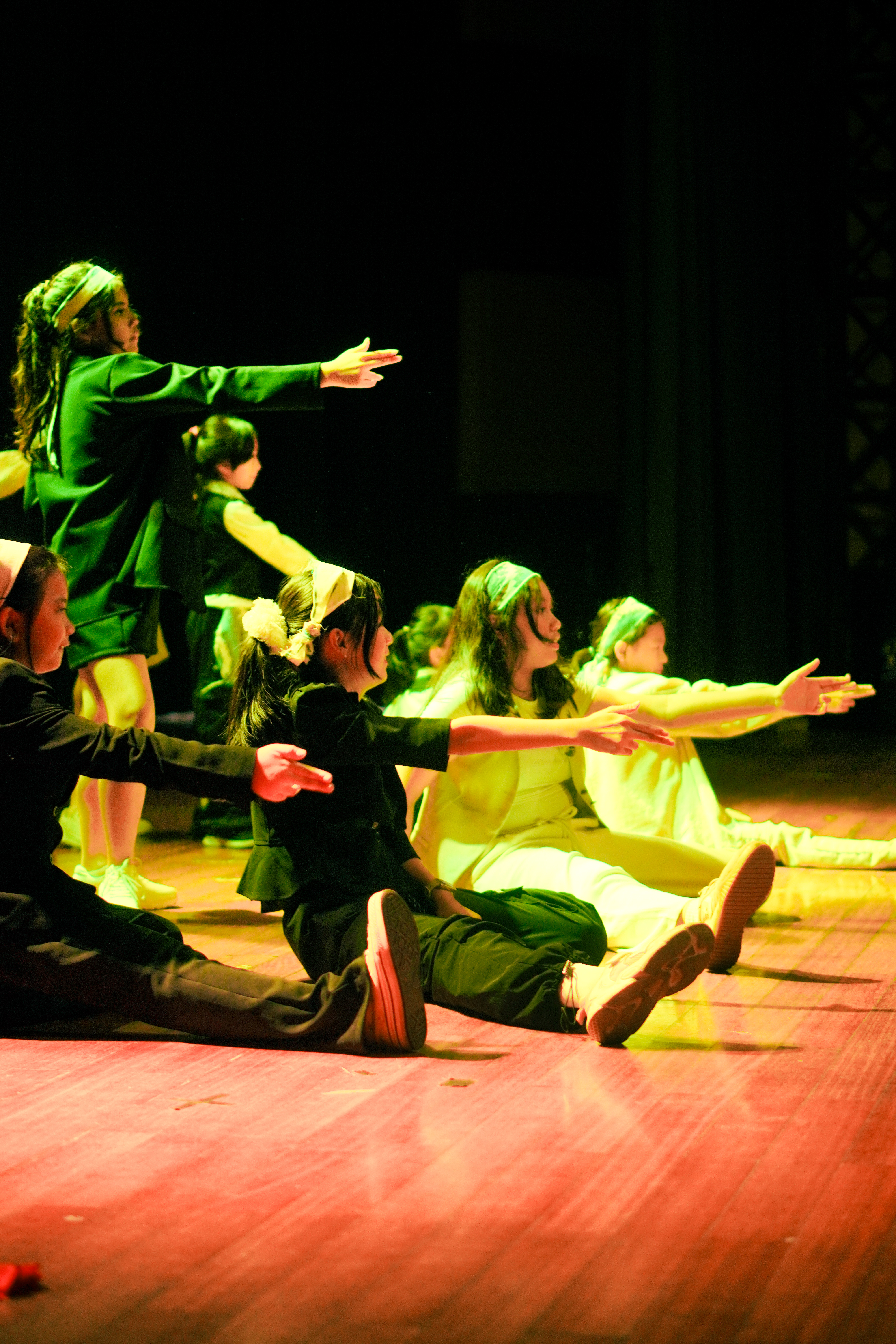 A large ensemble of dancers in green costumes reaching their arms outward in unison on stage at Jalantari 4.0